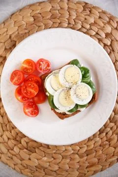 Top view on white dish with egg sandwich served with spinach and organic cher Stock Photos