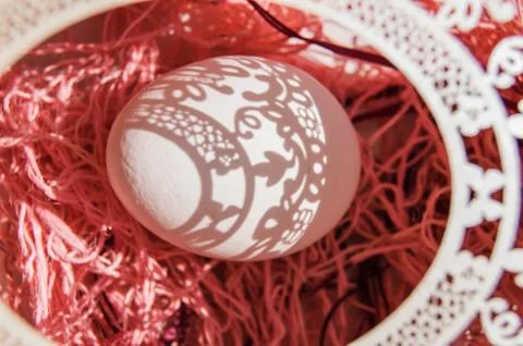 Top view of a white Easter egg in a paper openwork frame on a pink background Stock Photos