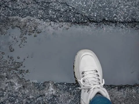 Top view of white leather boot near water puddle on grey asphalt. Early spr.. Stock Photos