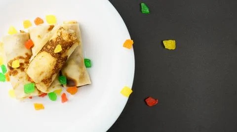 Top view of white plate with thin pancakes stuffed with candied fruits on bla Stock Photos