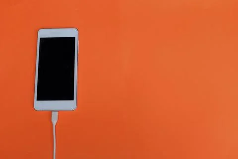 Top view white Smartphone Plug In with Charger Adapter on orange Background Stock Photos