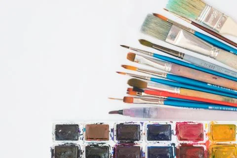Top view: on the white surface are watercolor paints and various brushes for  Stock Photos