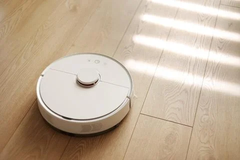 Top view of white wireless autonomous robotic vacuum cleaner on wooden floor. Stock Photos