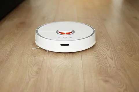 Top view of white wireless autonomous robotic vacuum cleaner on wooden floor Stock Photos