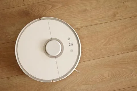 Top view of white wireless autonomous robotic vacuum cleaner on wooden floor. Stock Photos
