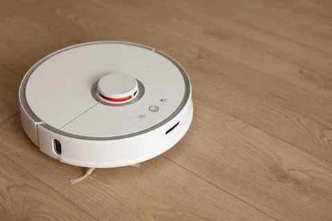 Top view of white wireless autonomous robotic vacuum cleaner on wooden floor. Stock Photos