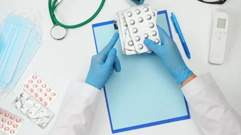 Top view on a white work desk of a doctor, doctor holds a stack of pills in a bl Stock Footage 146318225