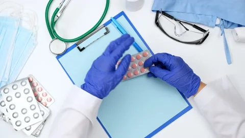 Top view on a white work desk of a doctor, doctor holds a stack of pills in a bl Stock Footage 146320380