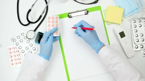 Top view on a white work desk of a doctor, doctor holds a stack of pills in a bl Stock Footage 150232103