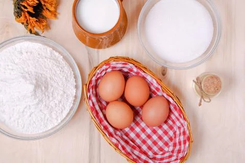 Top view: wicker basket of eggs, heap of flour, glass of milk, sugar, butter  Stock Photos