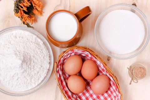 Top view: wicker basket of eggs, heap of flour, glass of milk, sugar, butter  Stock Photos