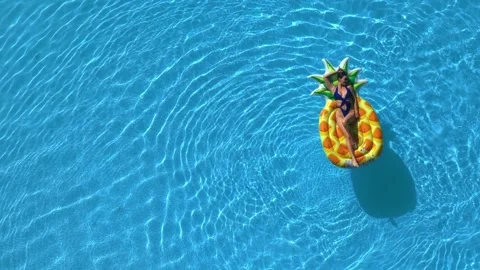 Top view of woman on a big pineapple float in a clear blue pool 動画素材 313071237