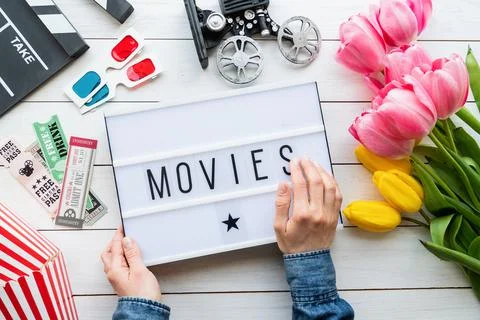 Top view of woman hands holding lightbox with word Movies, clapper board, tic Stock Photos