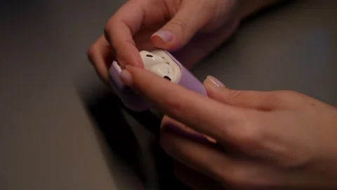 Top view of woman pulling white wireless earphone from stylish purple case Stock Footage 295639261