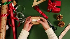 Overhead view of a woman using scissors, cutting green ribbon, making curly  ornaments while decorating a Christmas gift, wrapped in red wrapping paper.  Christmas time. Happy New Year. Diy present Stock Footage