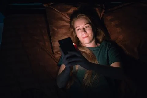 Top view of woman using mobile phone lying in bed at night having trouble sle Фото