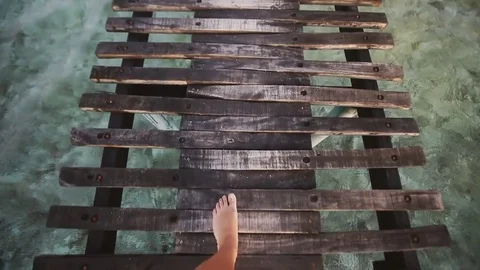 Top view of woman's bare feet stepping on the beautiful wooden path in the sea Stock Footage 80340189