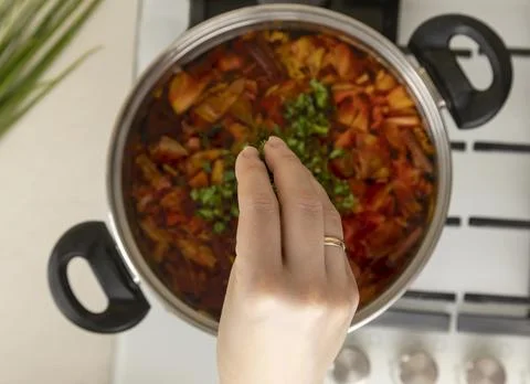 Top view of a woman's hand adding herbs to the cooked soup. Stock Photos