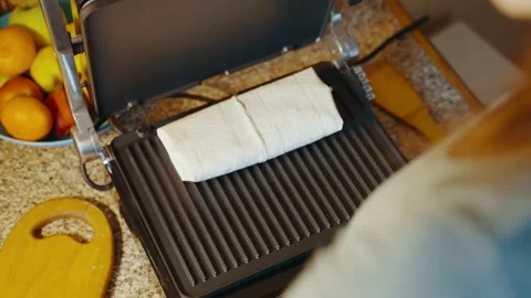 Top view of a woman's hand that moves stuffed pita bread on an electric grill Stock Footage 238952029