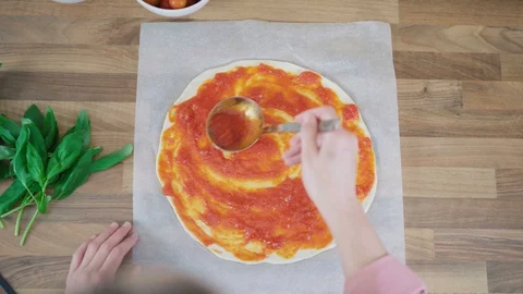 Top view of a woman's hands adding tomato sauce to a pizza dough on a wooden  Stock Footage 128202176