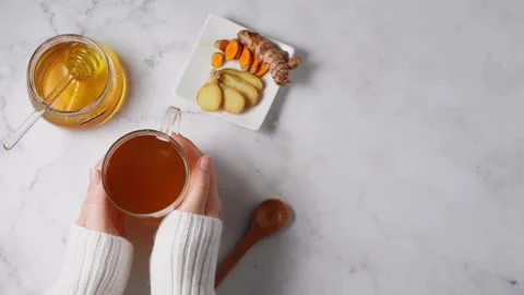 Top view of woman's hands adding honey into a tea cup with turmeric and ginger Video stock 138378261