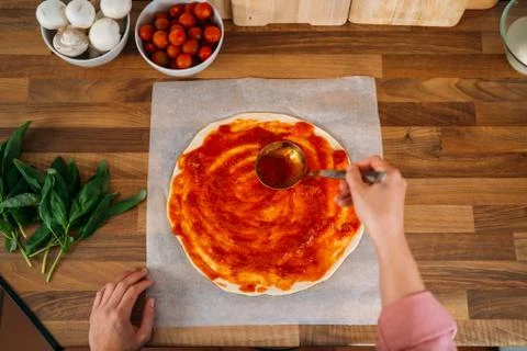 Top view of a woman's hands adding tomato sauce to a pizza dough on a wooden  Stock Photos