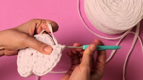 Top view of woman's hands crocheting with ribbon yarn on pink background Stock Footage 237115961