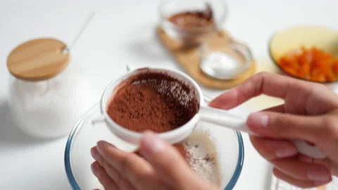 Top view of a woman's hands sifting cocoa through a sieve into a bowl of flo Stock Footage 213317374