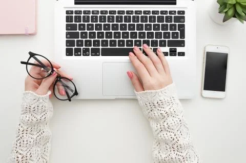 Top view of woman's hands typing on laptop keypad and holds eyeglasses on white Stock Photos