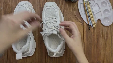Top view of women's hands pulling out shoelace from sports sneakers. Video stock 161825273