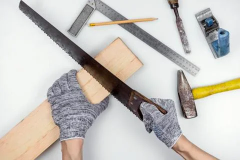 Top view of a work table in a carpentry workshop. Hands in gloves sawing a board Stock Photos