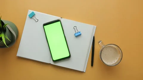 Top view of workspace with green screen phone notebook coffee cup and plant.. Stock Footage 332744785