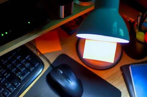 Top view on workspace at night with focus on orange sticky note and white lamp Stock Photos