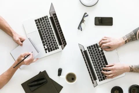 Top view of workspace with two laptops and male hands typing and writing in n 库存照片