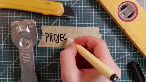 Top view of writing PROJECT PLAN on masking tape with minimalist tools. Stock Footage 337816333
