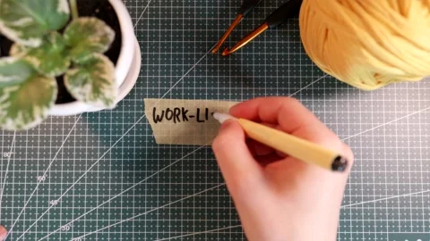 Top view of writing WORK-LIFE BALANCE on tape near knitting yarn and plant Stock Footage 338183923