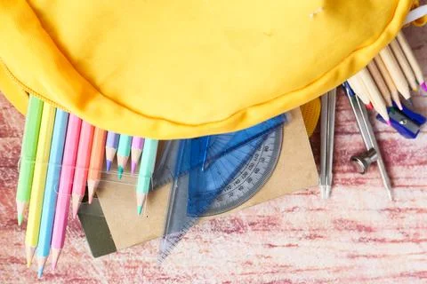 Top view of yellow backpack with different colorful stationery on table. Stock Photos