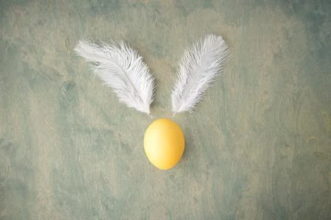 Top view of a yellow Easter egg and white feathers like the Easter bunny on.. Stock Photos