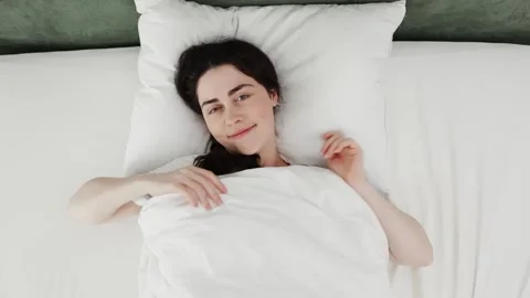 Top view of young Caucasian smiling woman who has woken up and looking at camera Stock Footage 250853585