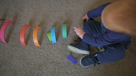 Top view of young child organizing colorful wooden toys in row on soft carpet Vidéo 295469816