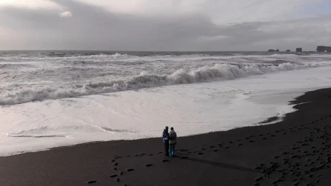 Top view of young couple standing on the black beach and looking on ocean in Stock Footage 106421305