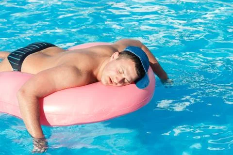 Top view of young drunk guy swim with pink circle in pool. drunk guy on vacat 写真素材