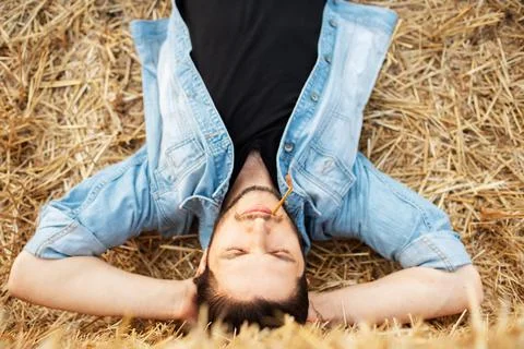 Top view of young guy with wheat spike in mouth lying on dry land. Stock Photos