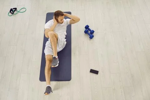 Top view of young man doing crunches on sports workout mat on wooden floor in Foto stock