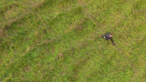Top view of young man going down the hill blanketetd with lush green grass Stock Footage 259435800