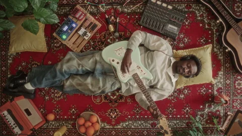 Top View of Young Man Lying on Vintage Rug, Playing Guitar with Eyes Closed Vídeo Stock 339849564