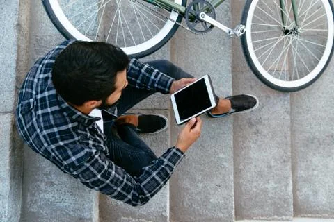 Top view on young man using a tablet while sitting on steps near the bike Stock Photos