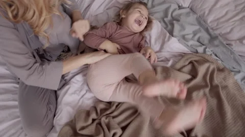 TOP VIEW: Young mom playing with little daughter on bed at home Vidéo 153976538