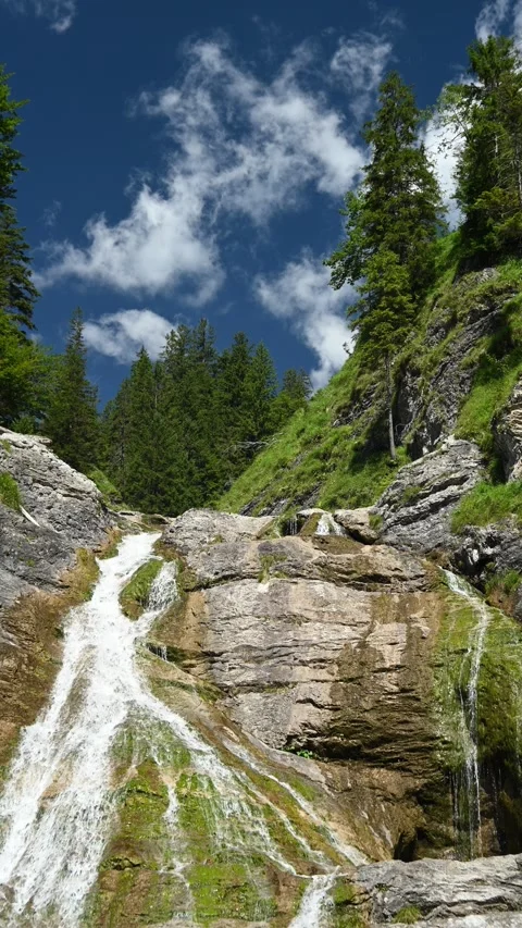 The top of a waterfall with trees and greens around, blue sky with white clouds Stock Footage 260875232