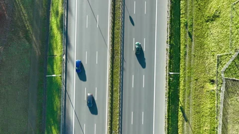 Top‑down aerial view of two parallel highway lanes with moving cars and grassy Stock Footage 321859868